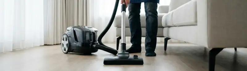 Professional house cleaner vacuuming a living room floor with a canister vacuum cleaner, Buffalo, NY.