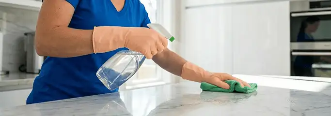 Maid service worker spraying and wiping a kitchen countertop with a microfiber cloth for sanitizing, Buffalo, NY.