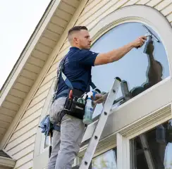 Professional window cleaner on a ladder using a squeegee to clean an exterior arched window, Buffalo, NY.