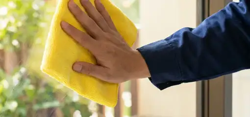House cleaner wiping a glass window with a yellow microfiber cloth for streak-free cleaning, Buffalo, NY.